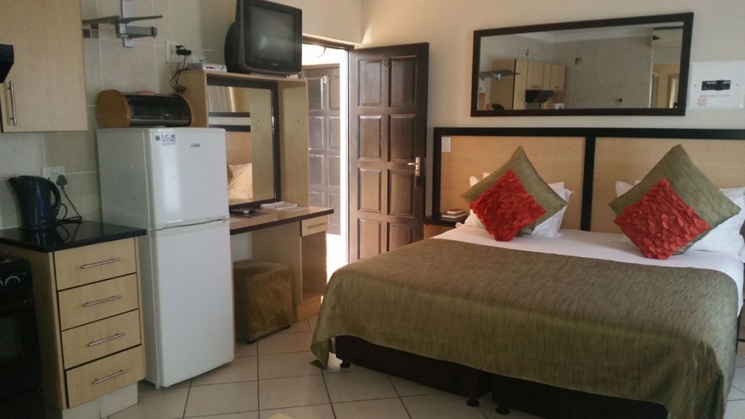 A hotel room with a bed, a television, a refrigerator, a desk, and a mirror.