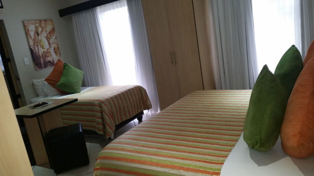 Habitación de hotel con dos camas, un escritorio y una silla. Hay cortinas en las ventanas y un cuadro en la pared.