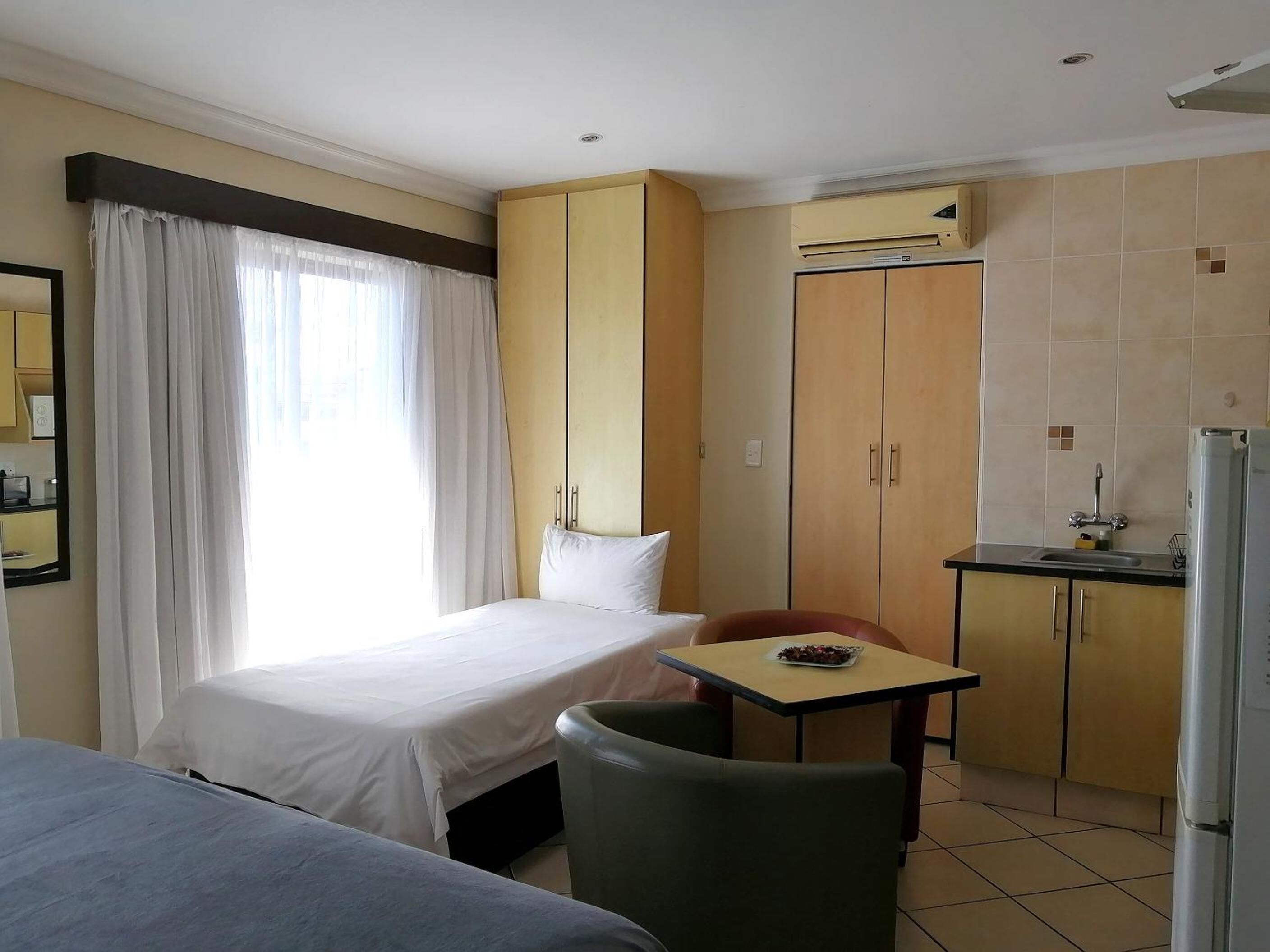 Ein kompaktes Hotelzimmer mit Bett, kleinem Tisch, Stuhl, Küchenzeile und Schrank.