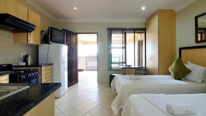 Une chambre d’hôtel avec une kitchenette, deux lits, une télévision et un balcon avec vue.