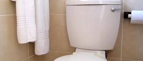 A white toilet with a tank, a towel rack with two towels, and a toilet paper holder.