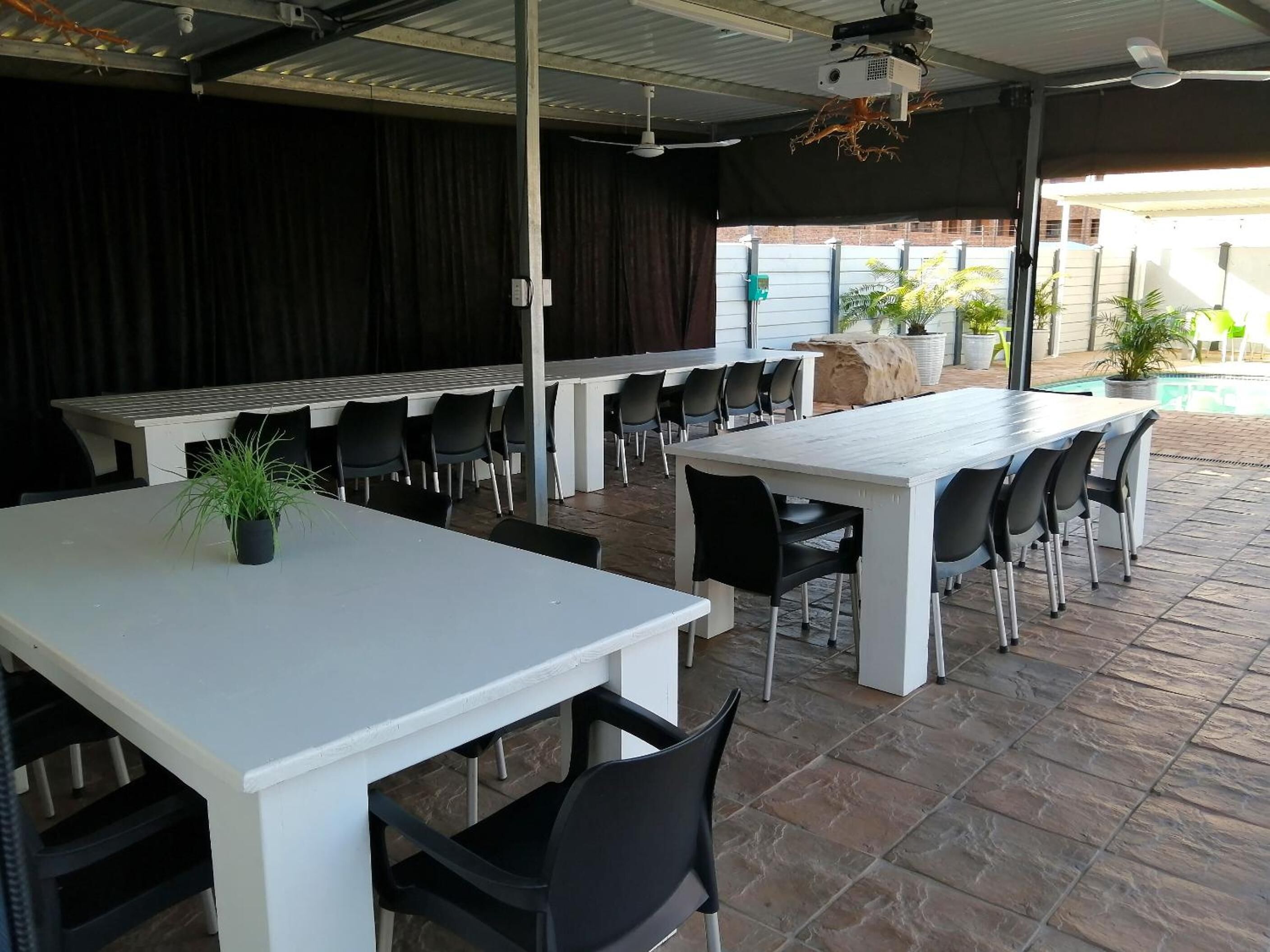 Un área de comedor al aire libre con varias mesas y sillas, un escenario y una piscina al fondo.