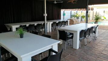 Un área de comedor al aire libre con varias mesas y sillas, un escenario y una piscina al fondo.
