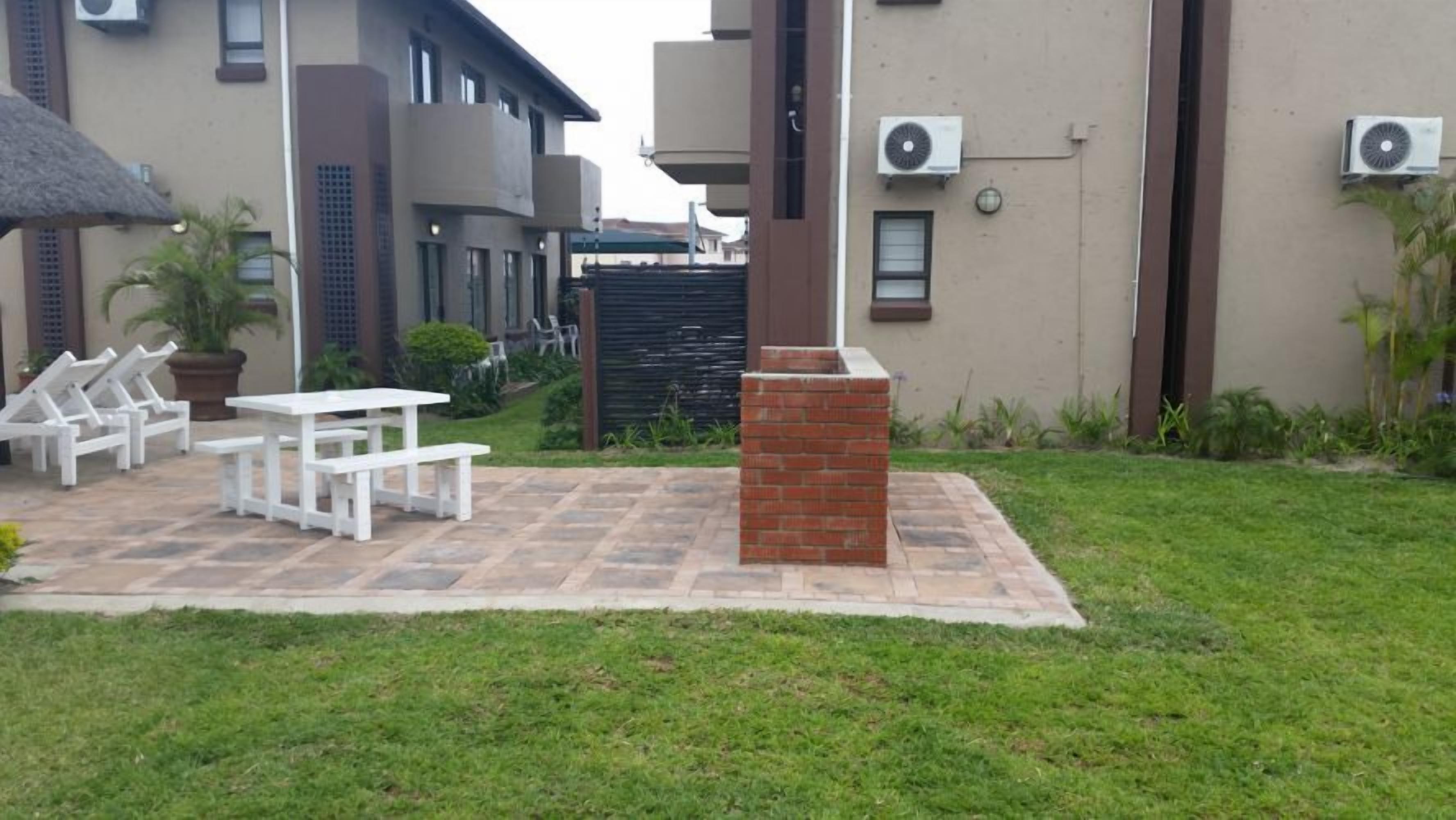A patio area with a table and chairs, a brick pillar, and air conditioning units on the building.