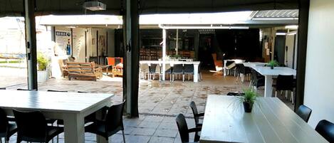 Um café ao ar livre com mesas, cadeiras, um espaço de bar e vista para a rua.