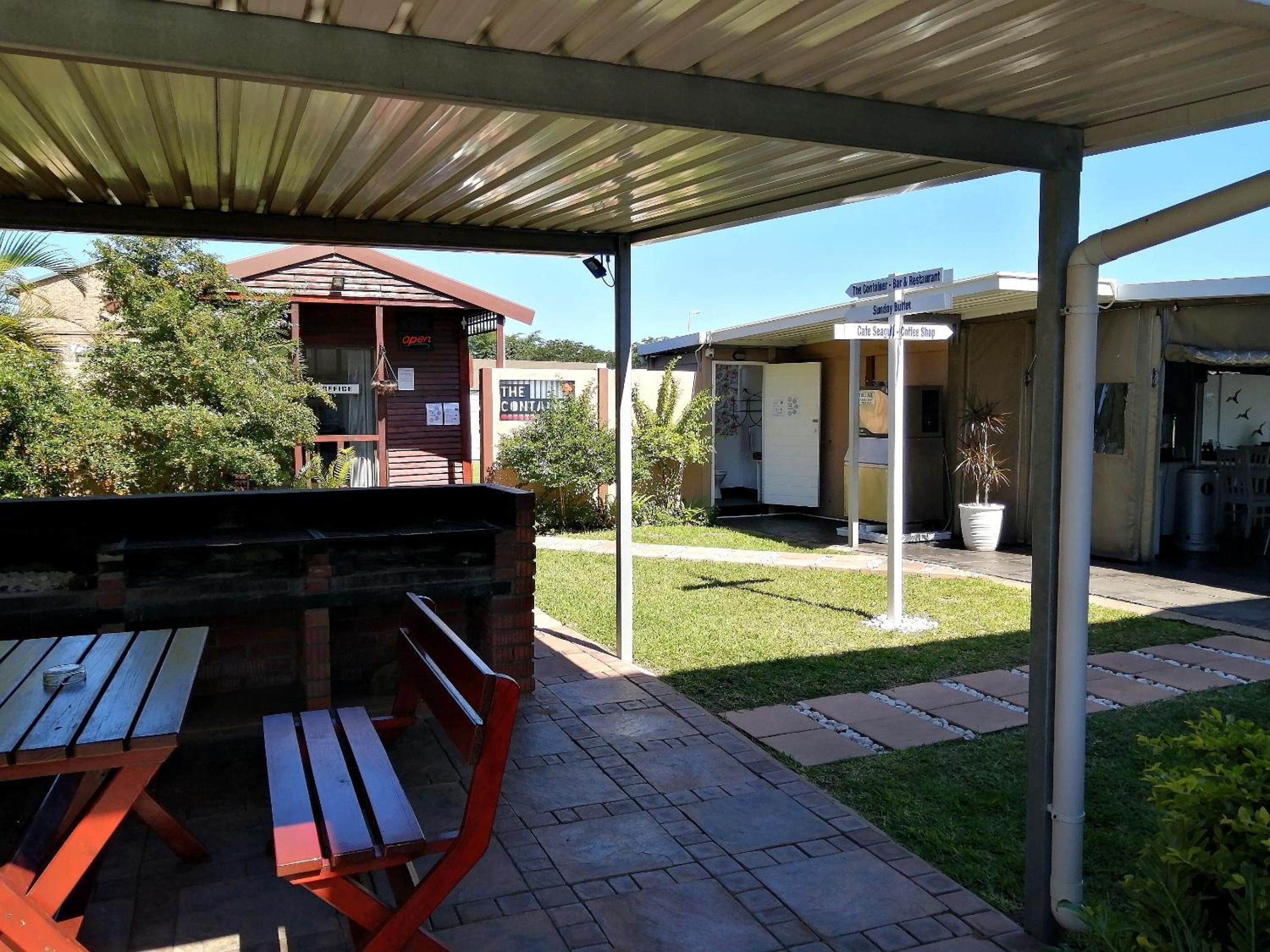 Un patio al aire libre con zona de estar cubierta, un pequeño edificio con un letrero y una planta en maceta.