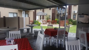An outdoor patio area with tables and chairs, a stone fountain, and a thatched umbrella. - Seagull Lodge (Richards Bay)