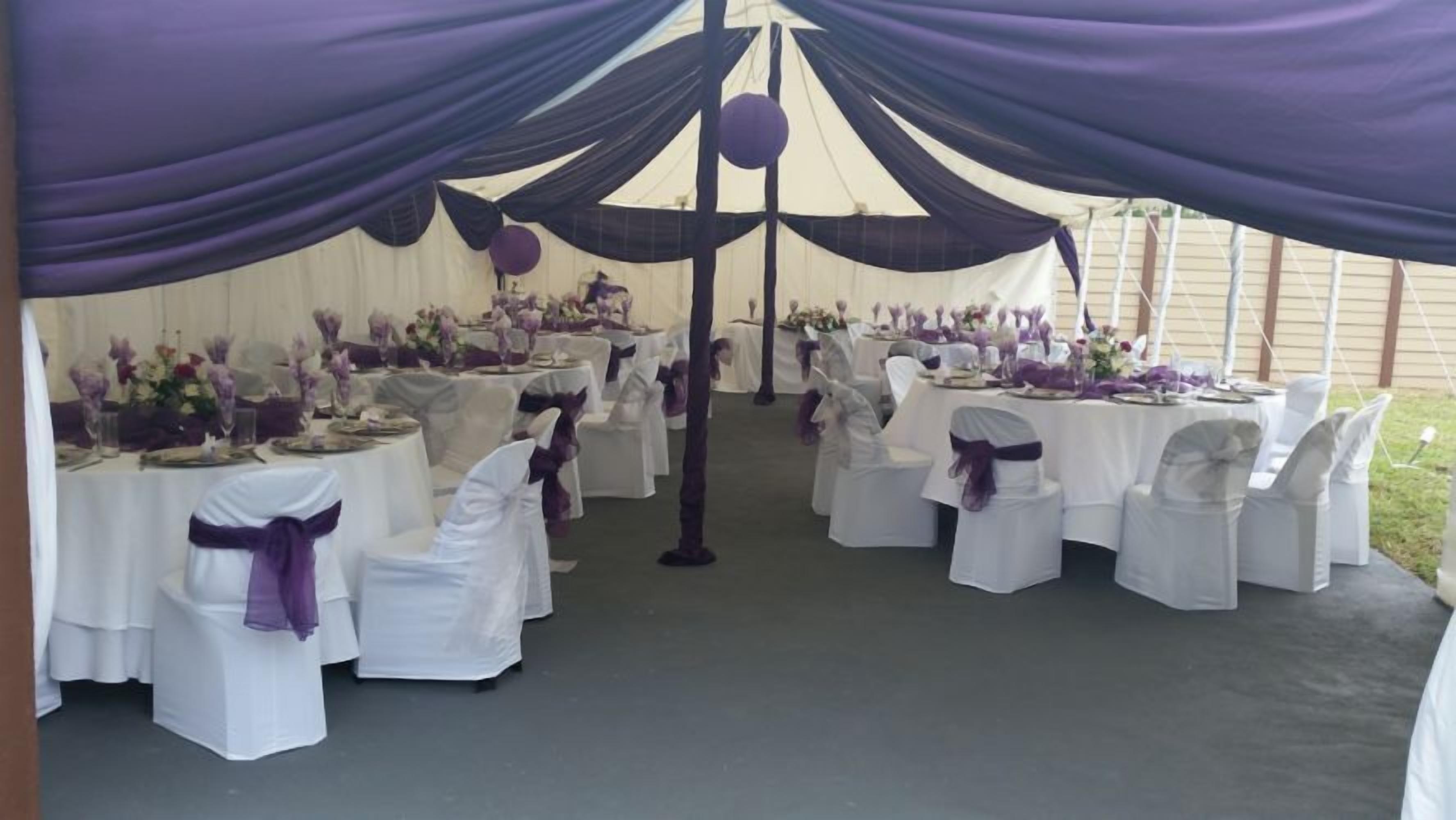 Un espace événementiel aménagé sous une tente, avec des tables dressées pour un événement formel, agrémenté de nappes blanches et de touches de couleur violette.