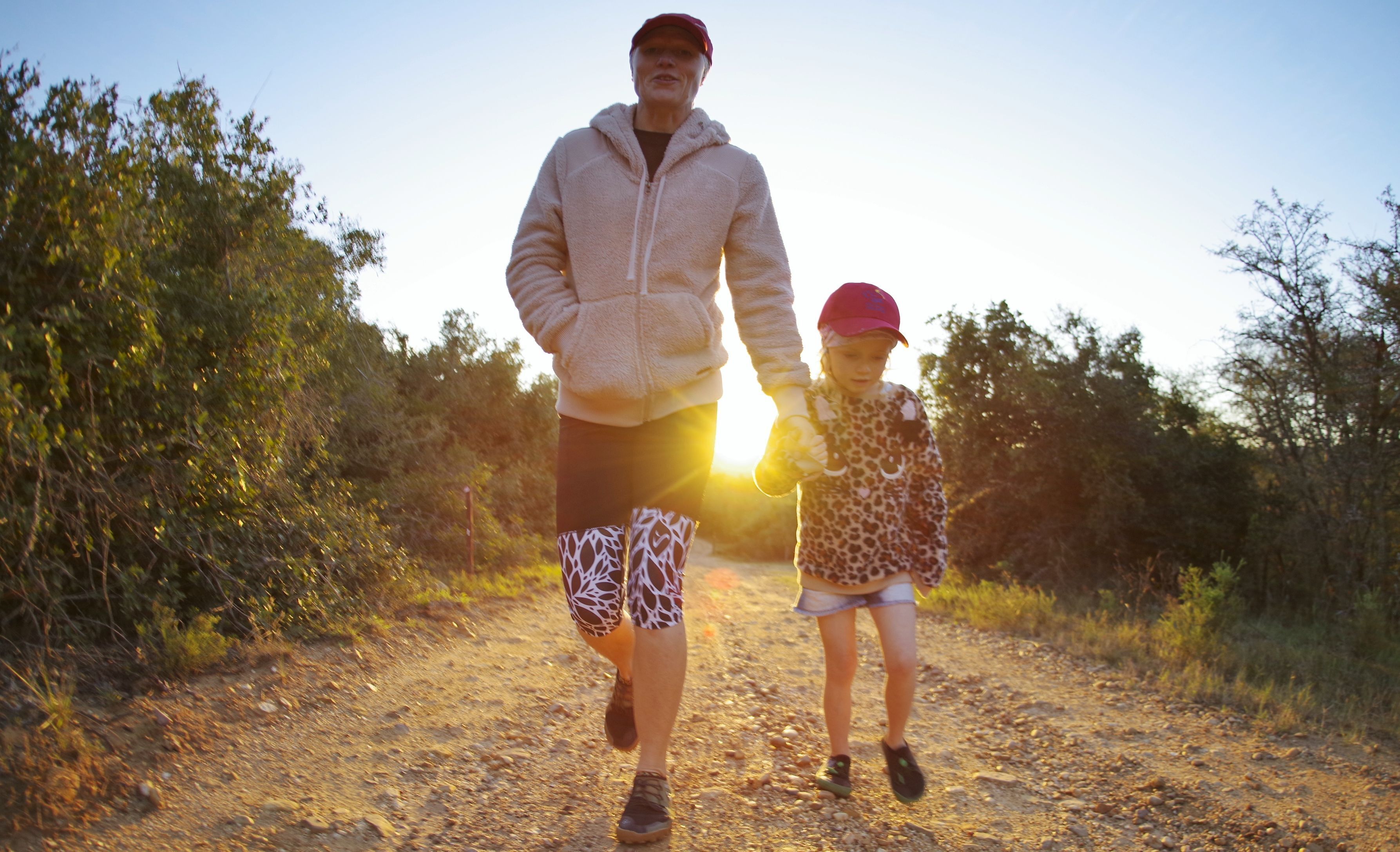 A man and a child walking on a dirt path surrounded by trees.