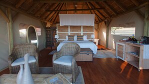 A room with a bed, two wicker chairs, a small table, a desk, and a view of the outdoors. - JBay Zebra Lodge (Thornhill)