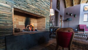 A stone fireplace with a fire, a red bucket chair, and a modern lamp. - JBay Zebra Lodge (Thornhill)
