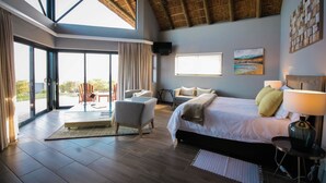 A spacious bedroom with a large bed, a seating area, and a balcony with a view. - JBay Zebra Lodge (Thornhill)