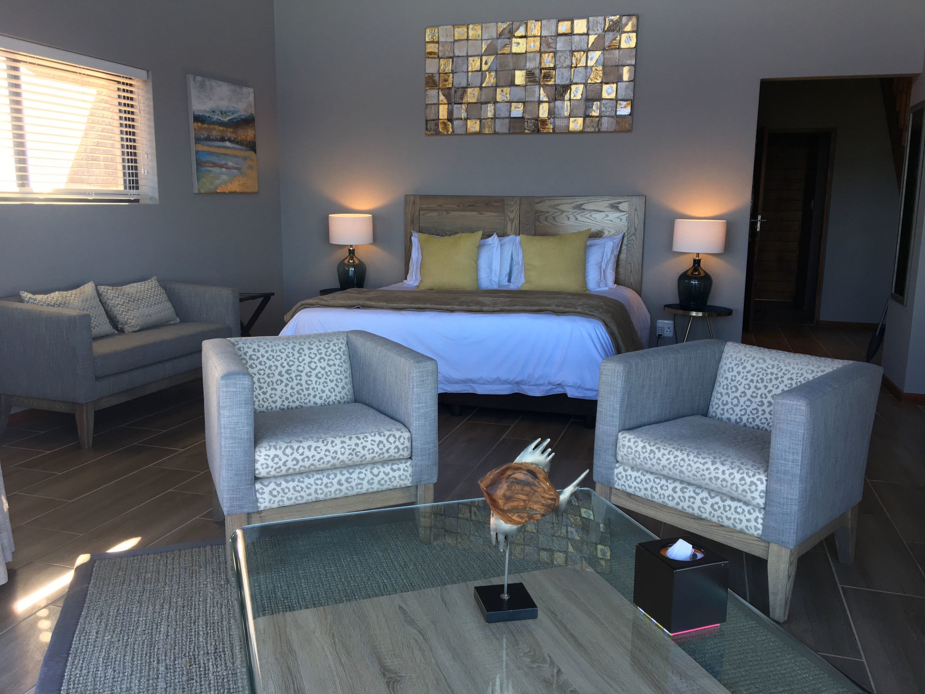 Une chambre d’hôtel moderne comprenant un lit, deux fauteuils, une table basse en verre et une fleur décorative.