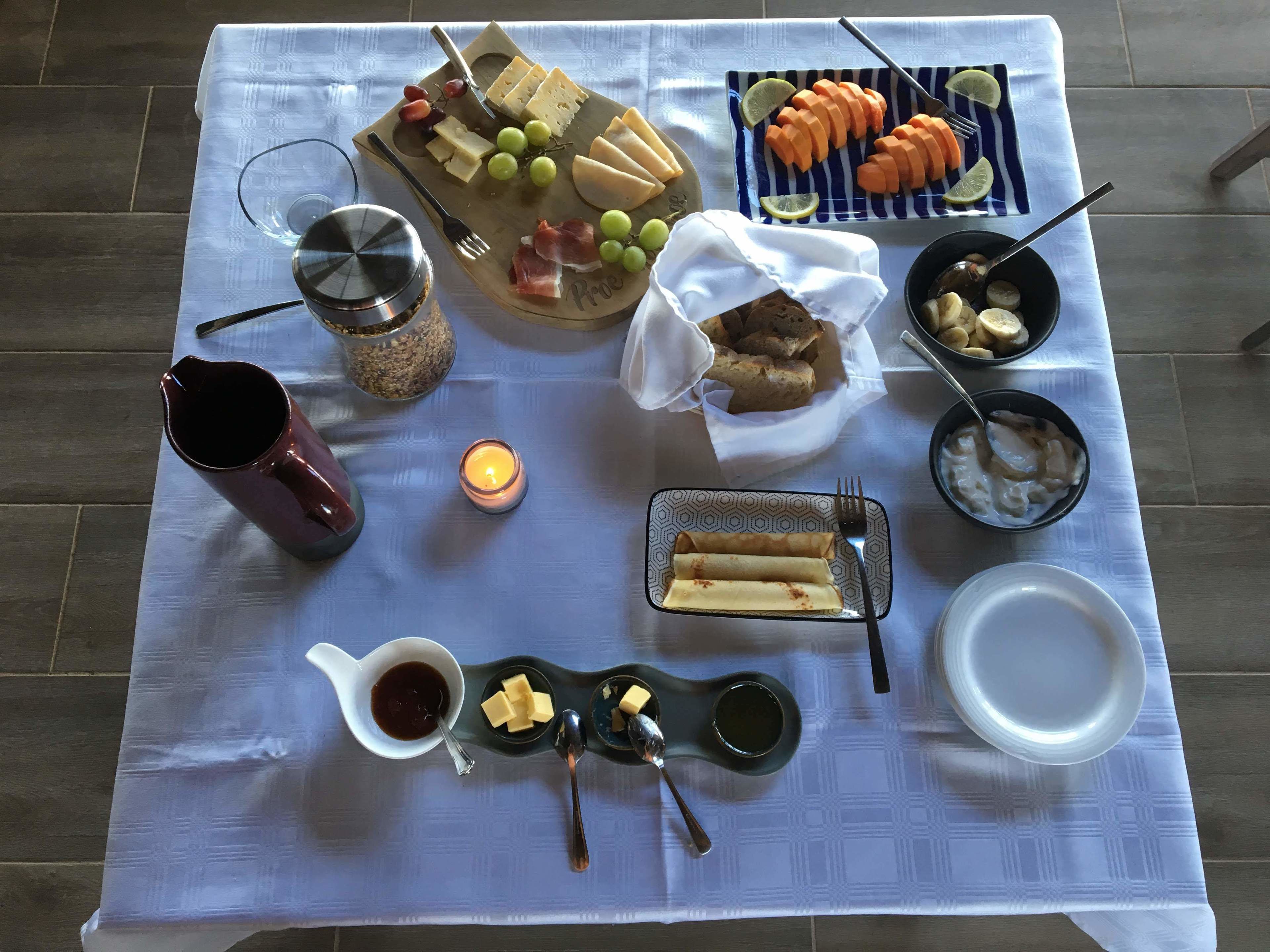 A table set with various food items, including cheese, grapes, and bread, along with condiments and a candle.