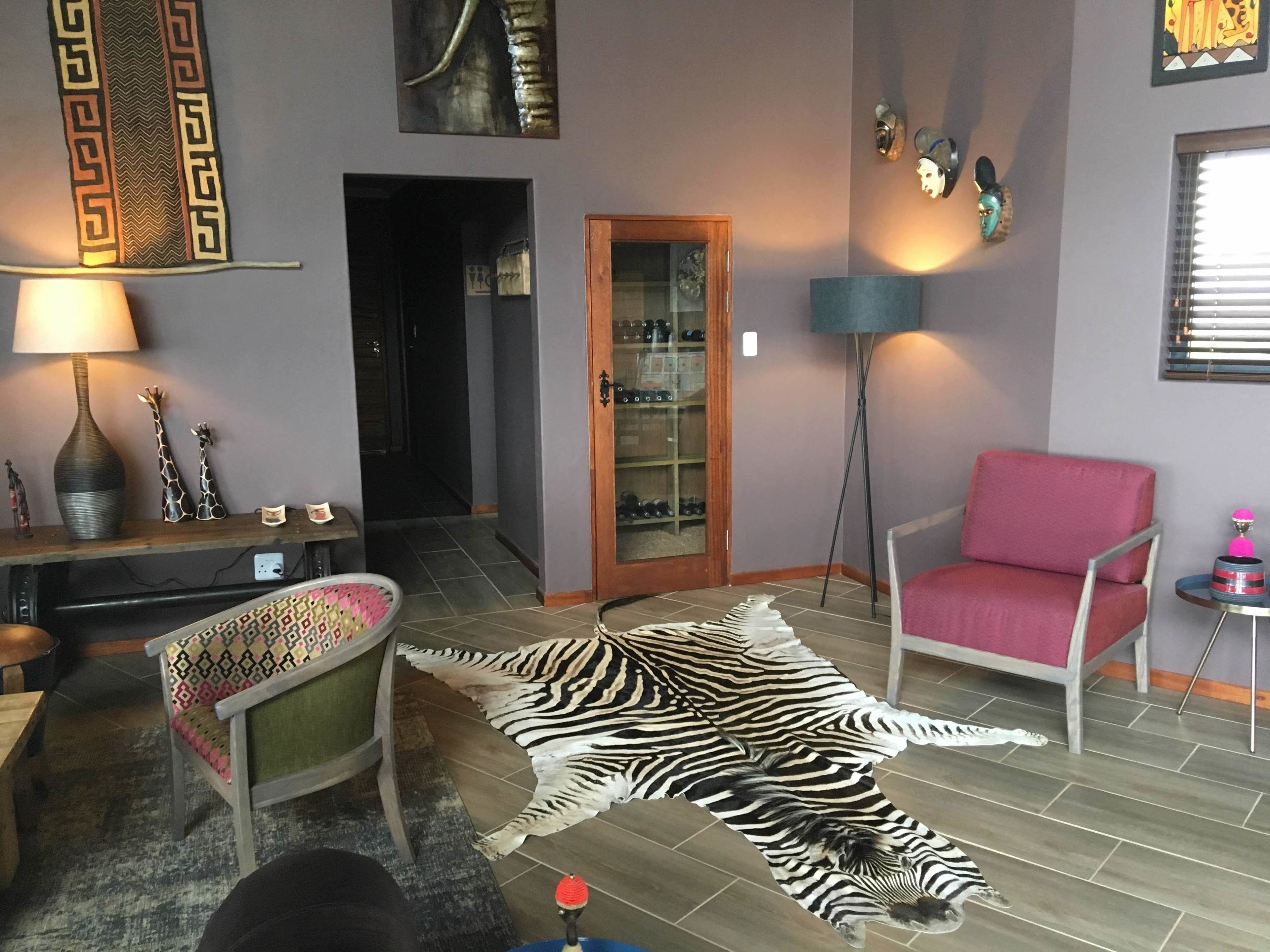 Un salon avec un tapis en peau de zèbre, un fauteuil rouge, une lampe et un meuble en bois contenant des chaussures.