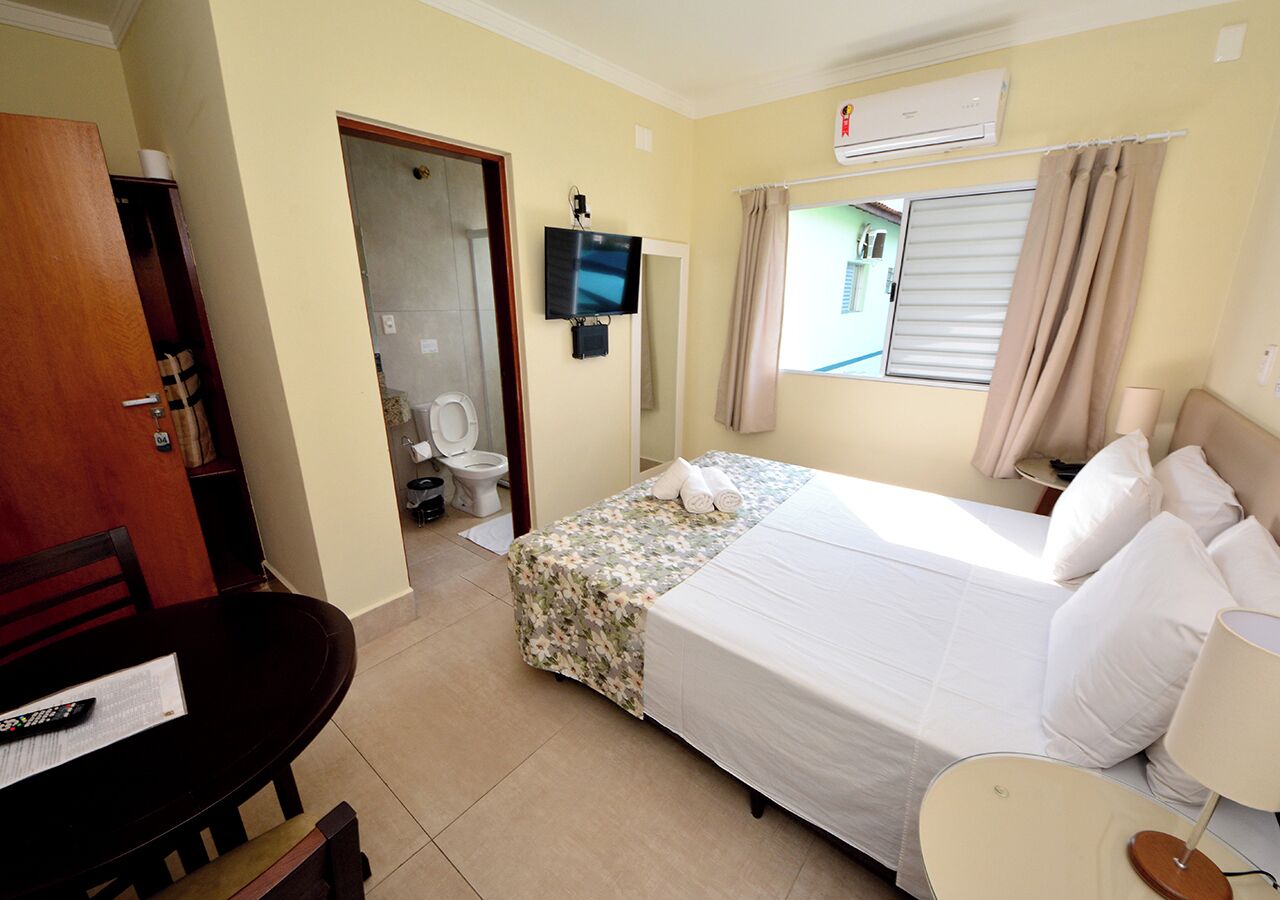 Quarto de hotel com cama, televisão, escrivaninha e banheiro.