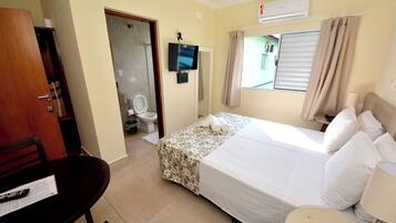 Quarto de hotel com cama, televisão, escrivaninha e banheiro.