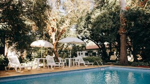 A swimming pool with white lounge chairs and umbrellas, surrounded by trees and a building in the background. - Hotel Passaledo (Indaiatuba)