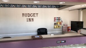 A reception desk at the Budget Inn with a sign above it, a black office chair, a shelf with snacks, and a TV on the right. - Budget Inn (Jasper)