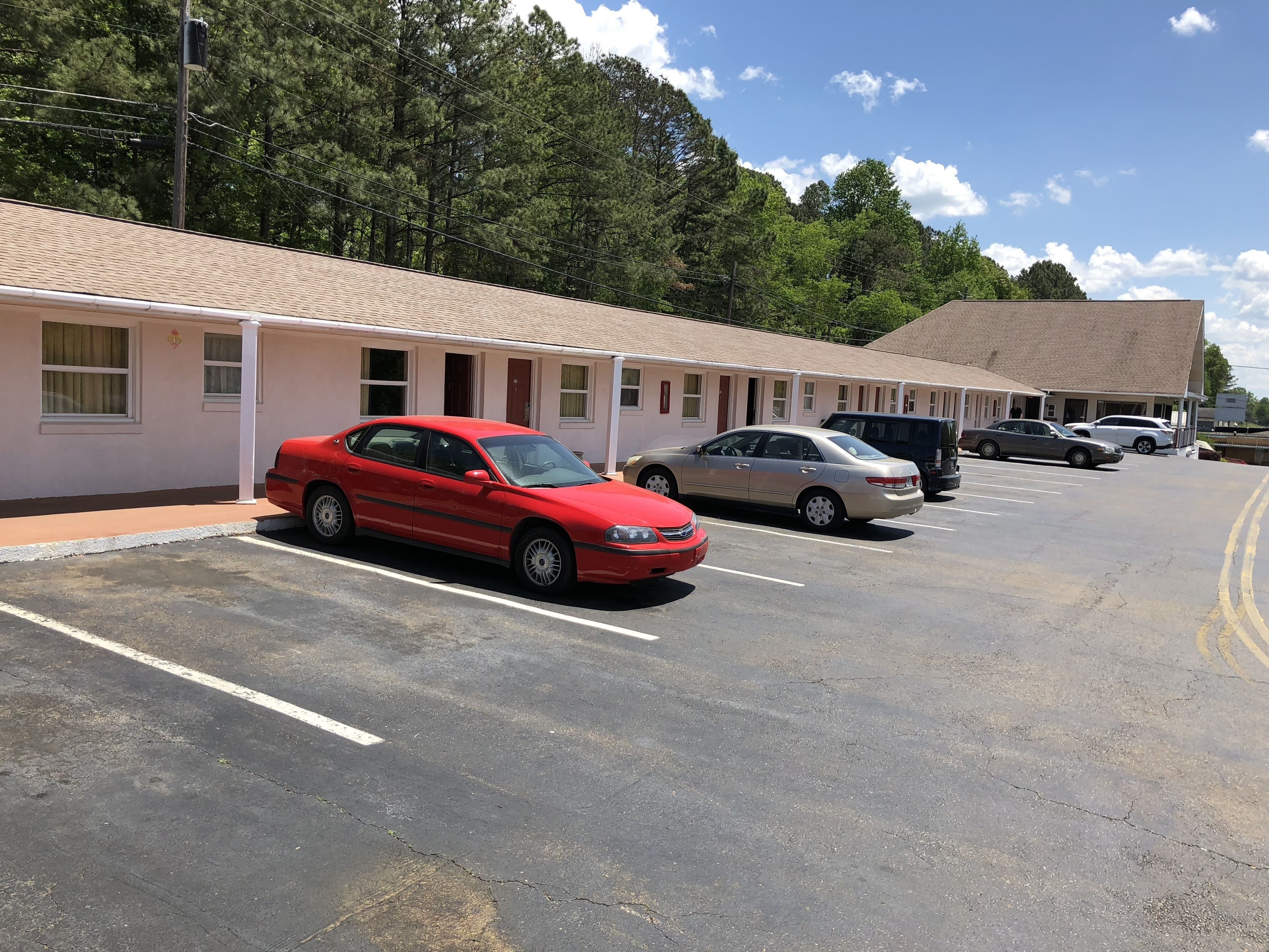 A row of motel rooms with a parking lot in front.