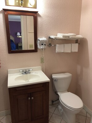 A bathroom with a white sink, wooden cabinet, and a toilet. There is a towel rack with towels and a hairdryer on the wall.