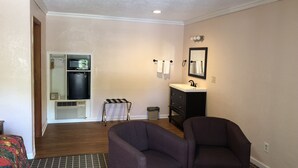 A compact living room with a sofa, a small table, a refrigerator, a sink, and a trash can. - Budget Inn (Jasper)