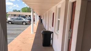 A covered walkway with a trash bin, a door, and a parking lot in the background. - Budget Inn (Jasper)