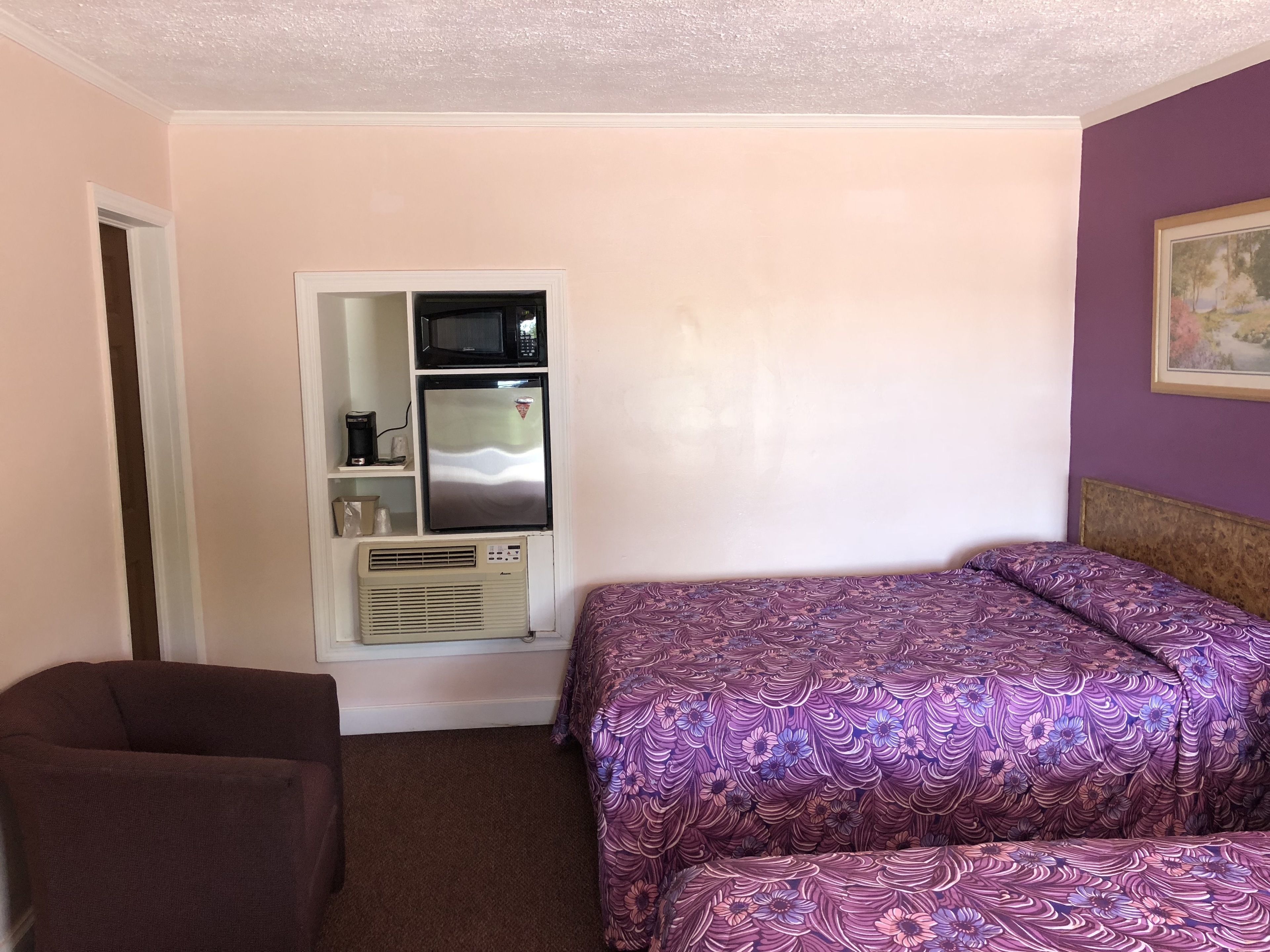 A bedroom with a bed, a chair, a wardrobe, and a microwave.