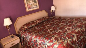 A bedroom with a bed, a nightstand, a lamp, and a framed picture on the wall. - Budget Inn (Jasper)