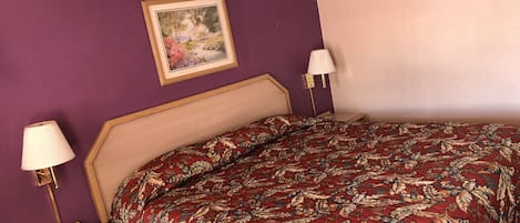 Et soveværelse med en seng, et natbord, en lampe og et billede i ramme på væggen.
