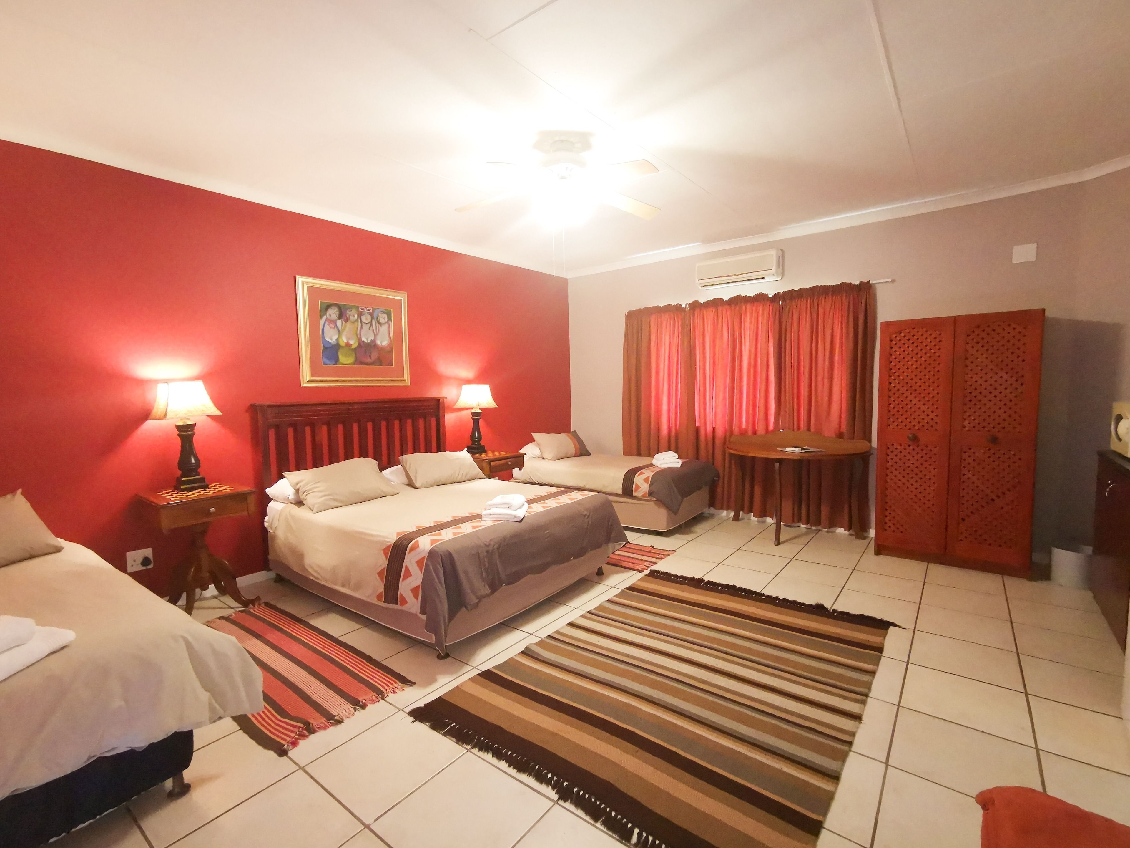 Habitación de hotel con pared roja, cama, escritorio, silla y armario.