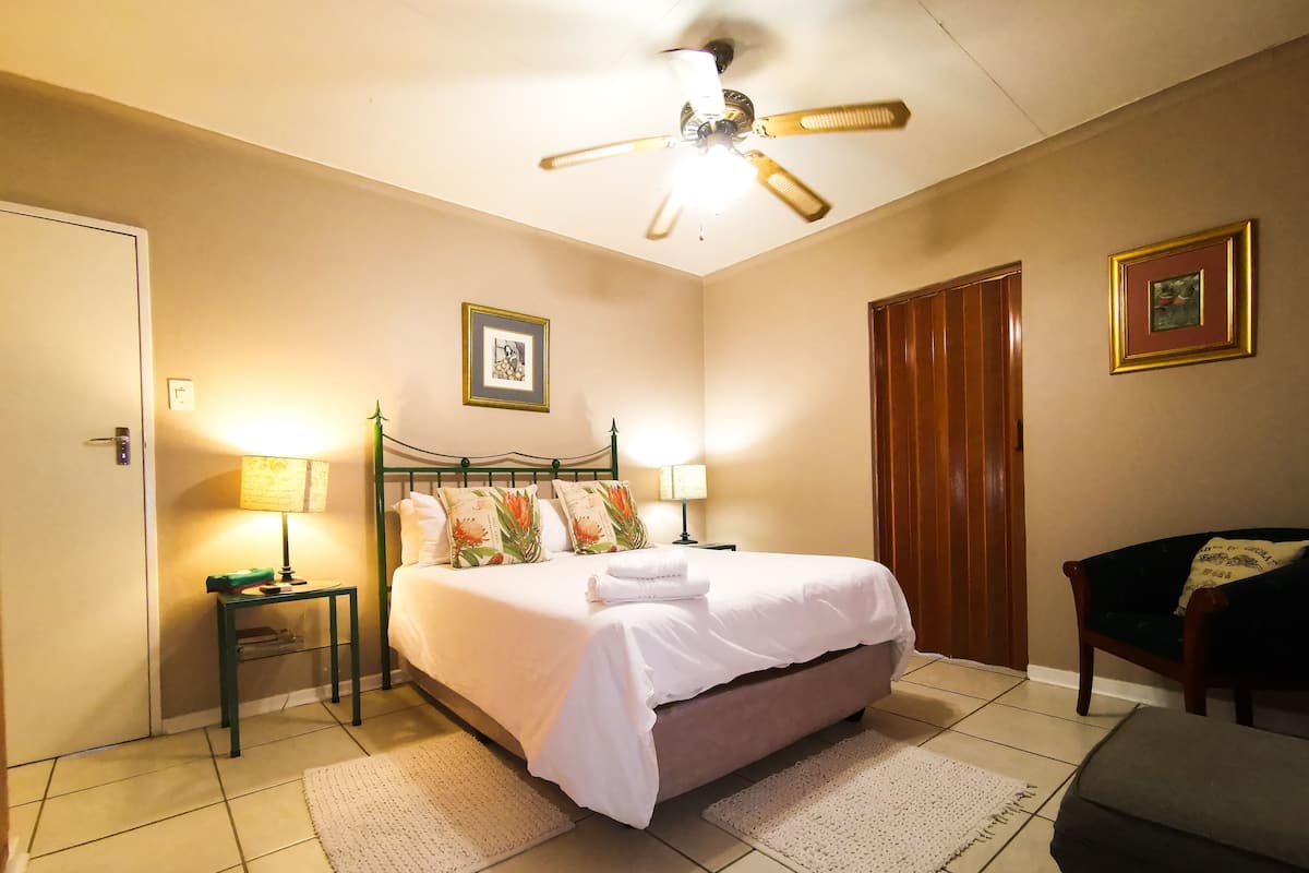 A neatly arranged hotel room with a bed, bedside lamps, a ceiling fan, a door, and a chair.