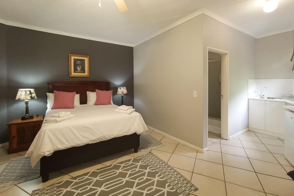 A bedroom with a bed, two bedside tables with lamps, a ceiling fan, a framed picture on the wall, and a view into the adjacent bathroom.