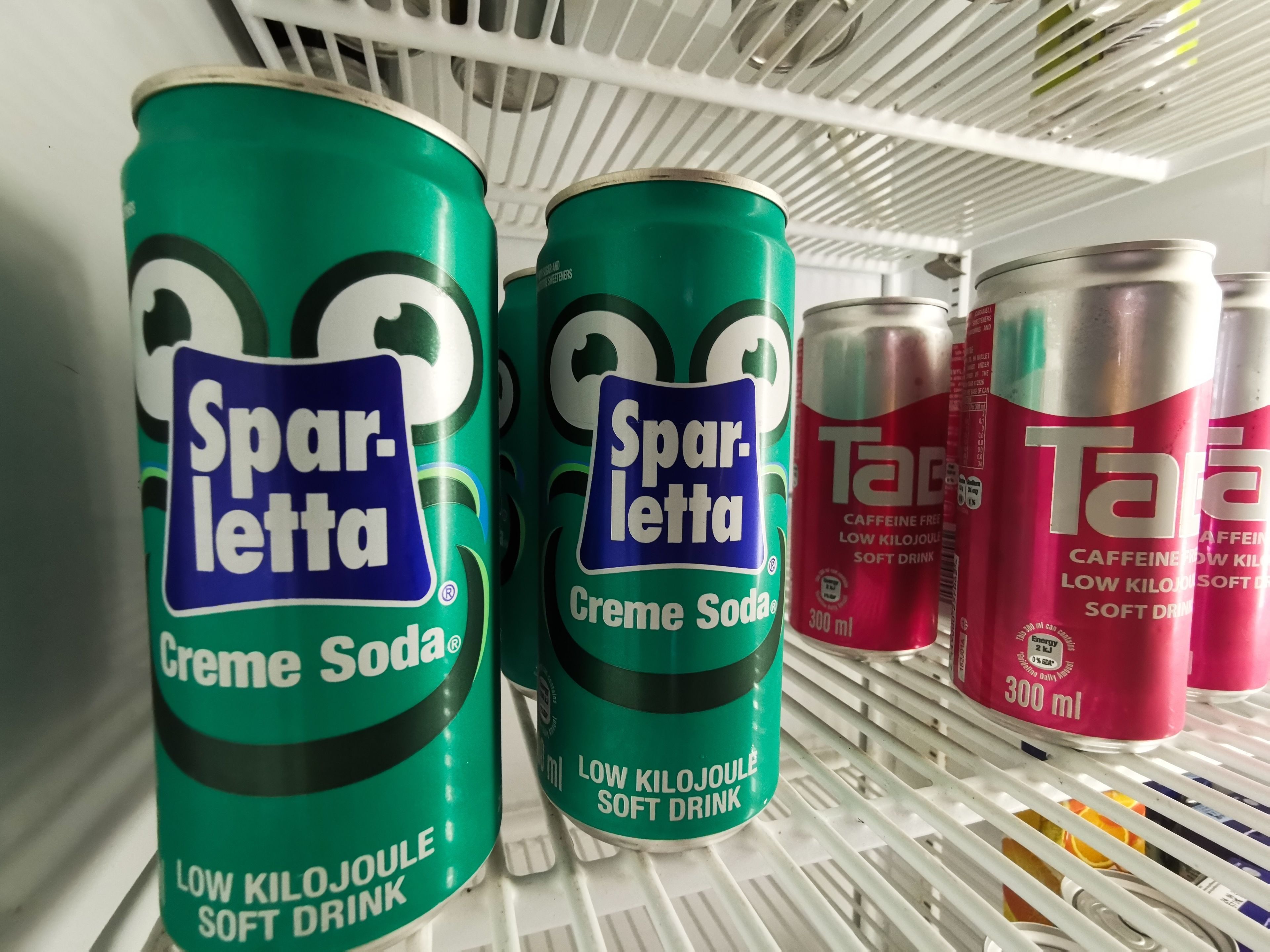 Un estante con tres latas de Sparletta Creme Soda y una lata de Tar.