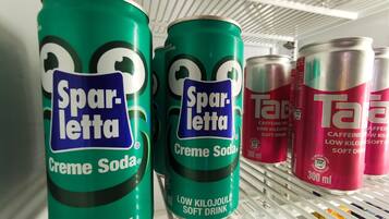 Un estante con tres latas de Sparletta Creme Soda y una lata de Tar.