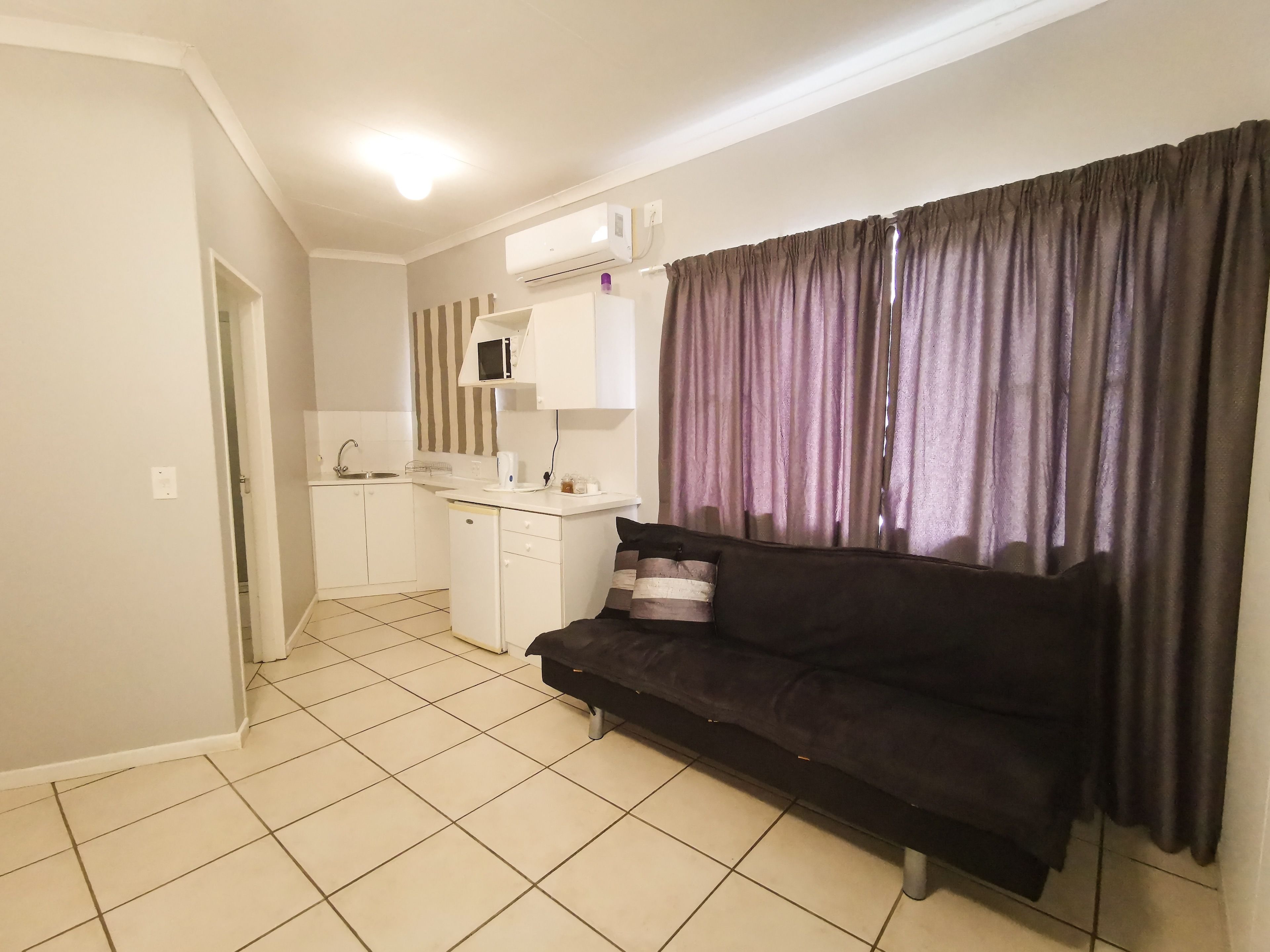 A compact living space with a kitchenette, a dark sofa, and a window with curtains.
