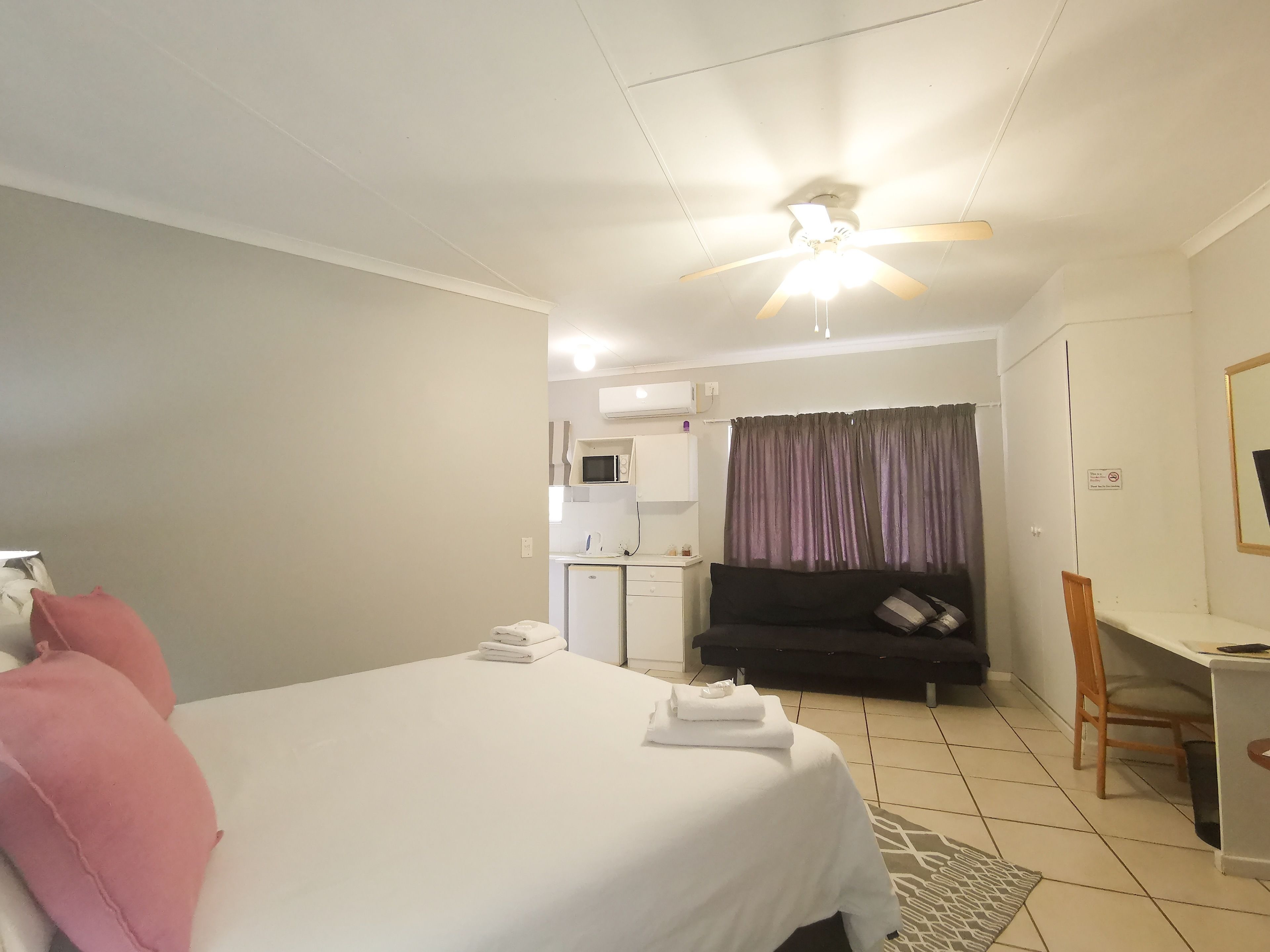 Una habitación de hotel con cama, escritorio, silla, kitchenette y baño.