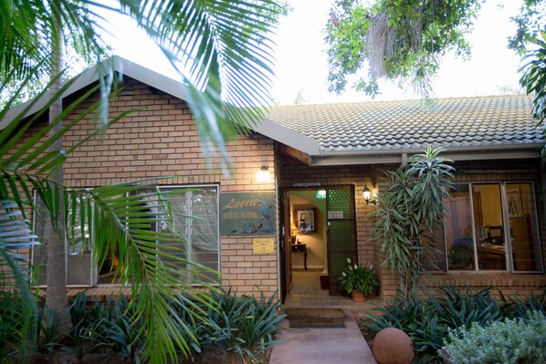 A guest house with a brick exterior, a tiled roof, and a signboard. - Loerie Guesthouse (Hoedspruit)