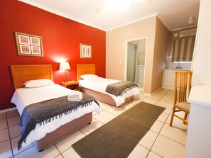 A hotel room with two beds, a small kitchenette, and a bathroom with a shower. - Loerie Guesthouse (Hoedspruit)