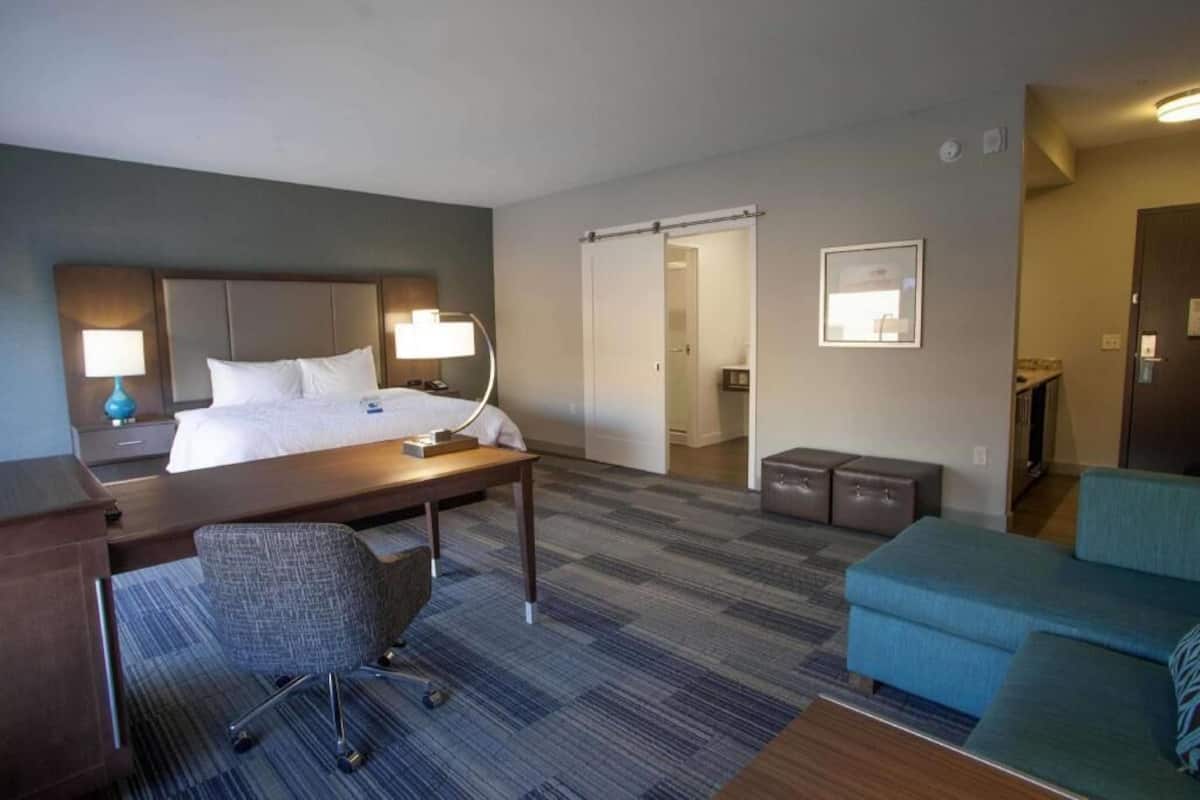A hotel room with a bed, desk, chair, sofa, and a sliding door leading to a bathroom.