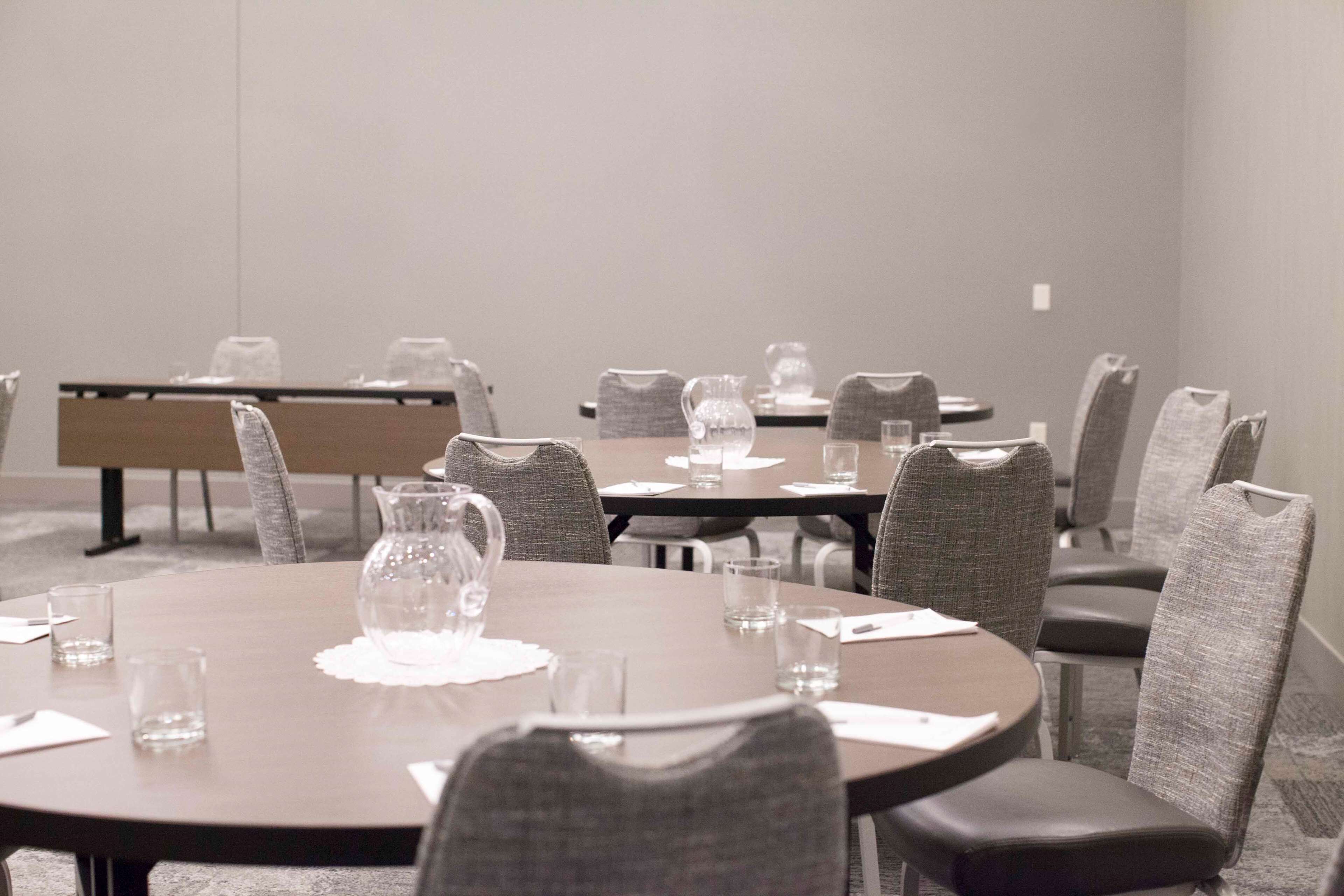 Une salle de conférence avec des tables rondes, des chaises rembourrées de couleur grise et des carafes à eau en verre transparent sur chaque table.