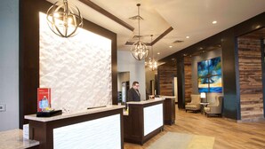 A reception area with a modern design, featuring a reception desk, a large abstract painting, and a seating area with two chairs and a table. - Hampton Inn & Suites Downtown St. Paul (St. Paul)