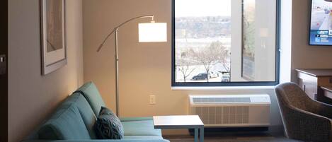 Habitación de hotel moderna con sofá, una mesita, lámpara de pie y un ventanal con vista a la ciudad.