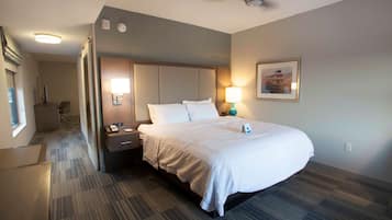 A hotel room with a large bed, a desk with a lamp, a phone, and a framed picture on the wall.