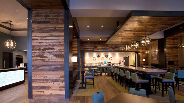A modern restaurant with wooden accents, a bar area, and multiple seating options. - Hampton Inn & Suites Downtown St. Paul (St. Paul)