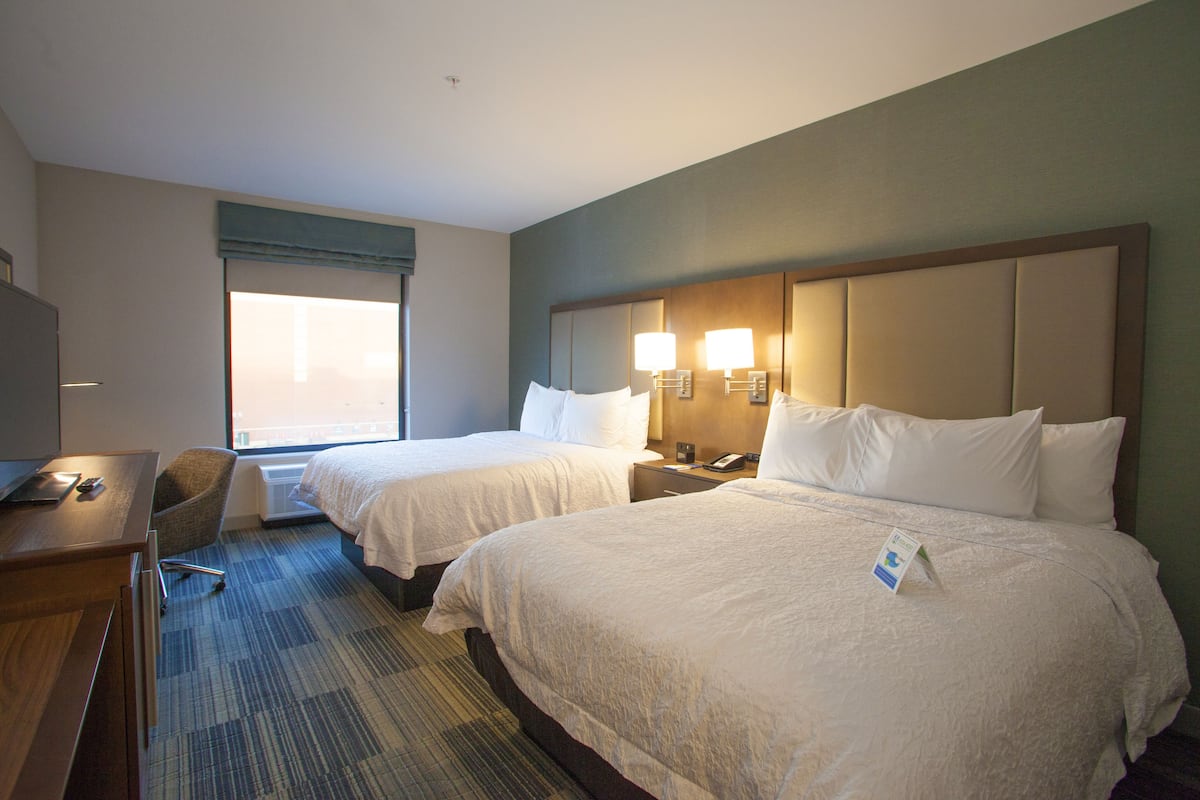 A hotel room with two beds, a desk, a chair, and a window with blinds.