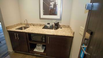 A compact kitchen with a granite countertop, a built-in microwave, a coffee maker, and a sink.