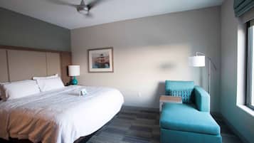 Una habitación de hotel con una cama grande, un escritorio, una silla, un ventilador de techo, una lámpara y una ventana.