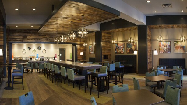 A restaurant with a long counter, multiple tables, and chairs. There are hanging lights and artwork on the walls.