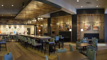 A restaurant with a long counter, multiple tables, and chairs. There are hanging lights and artwork on the walls.